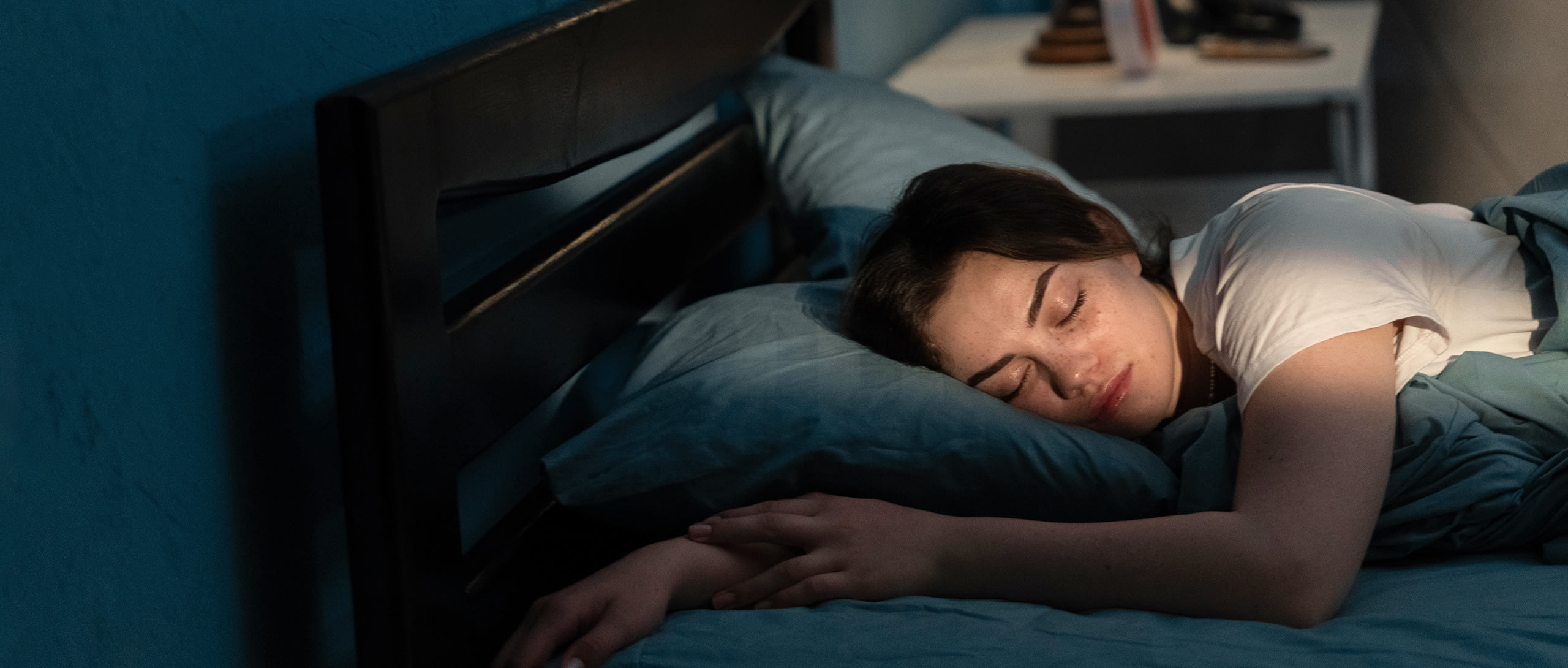 A young woman asleep in bed with blue covers.