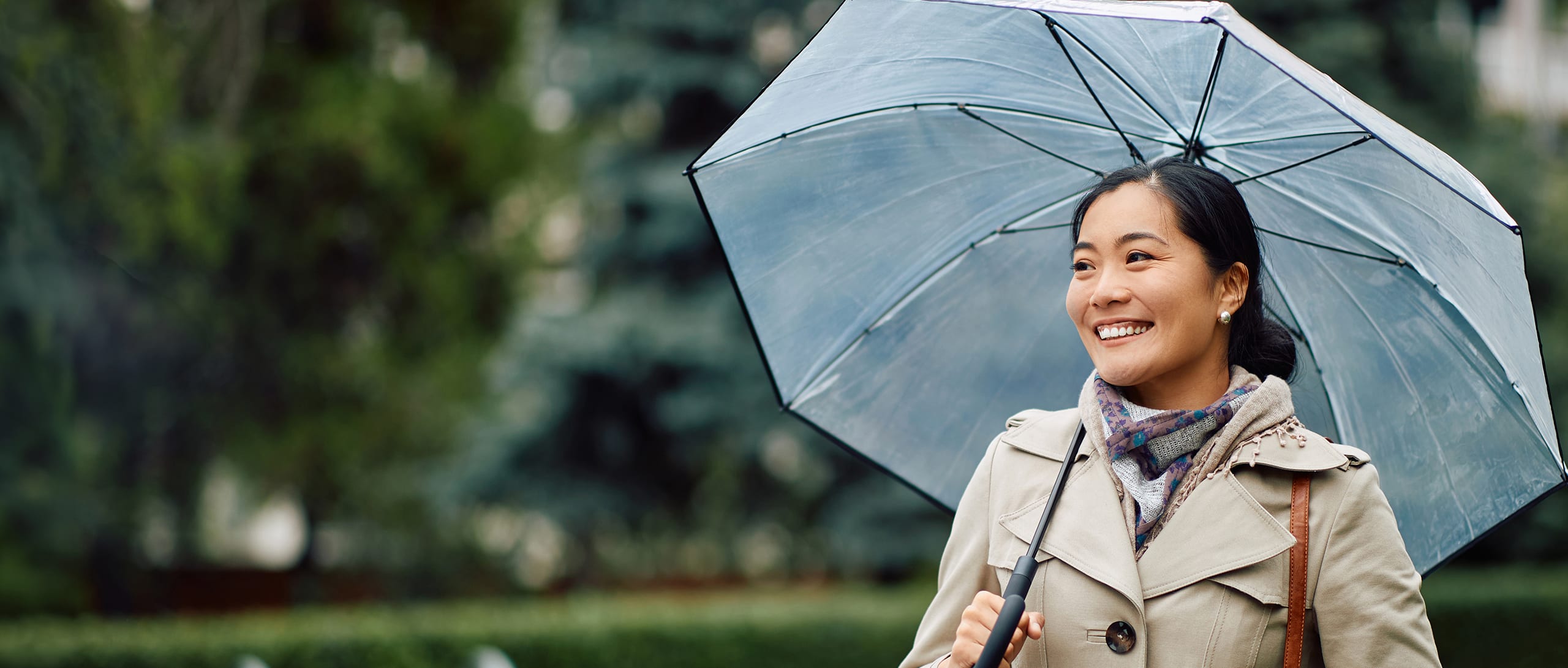 A woman smiling while holding an umbrella outside.