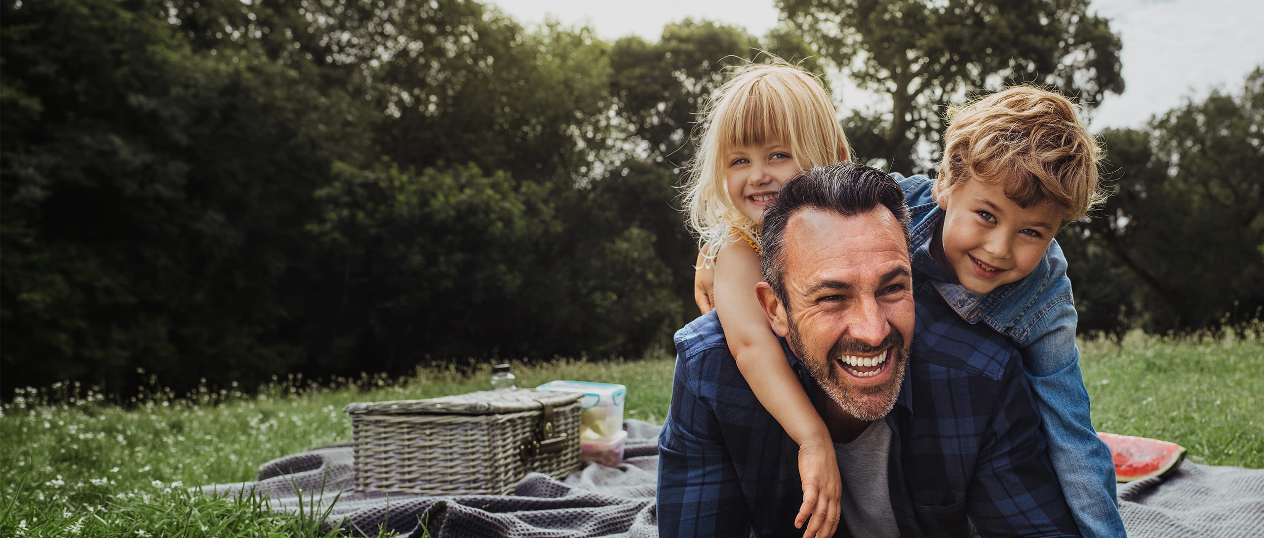 A father and his young children wearing blue and having fun at a picnic.