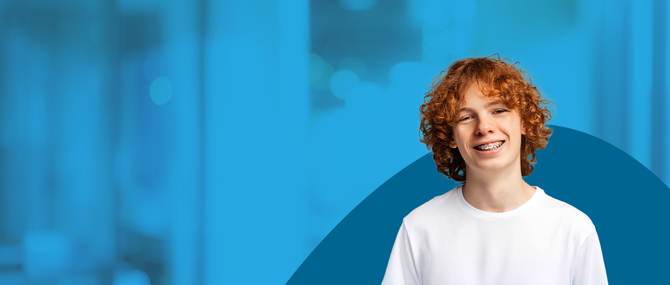 A young boy with curly red hair is smiling and showing off braces.