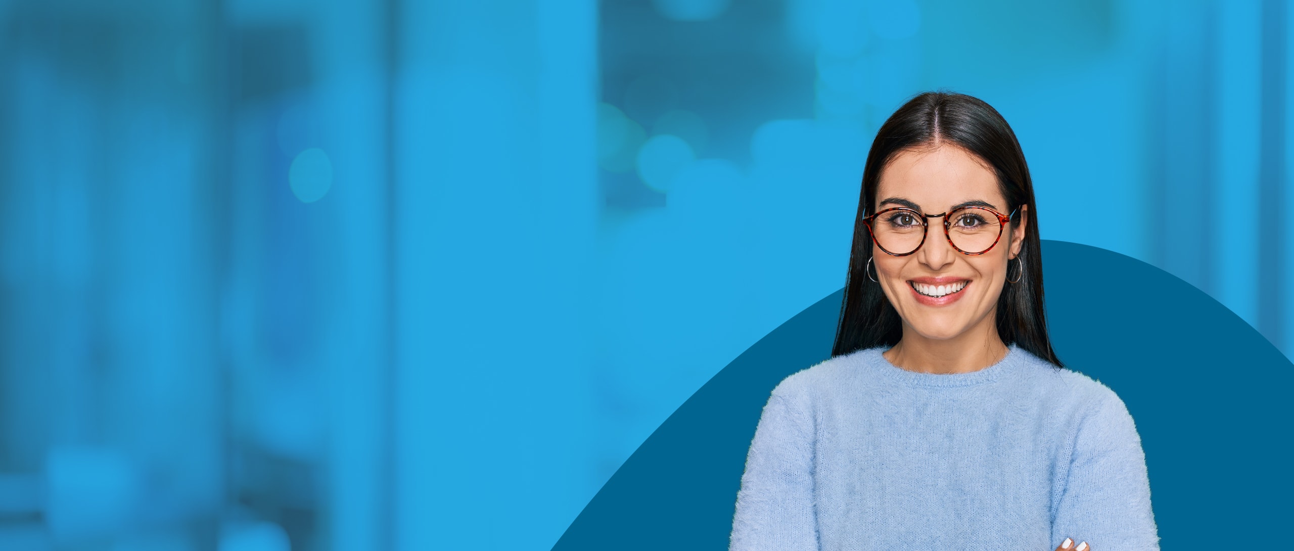A woman wearing a fuzzy blue sweater and round glasses is smiling.