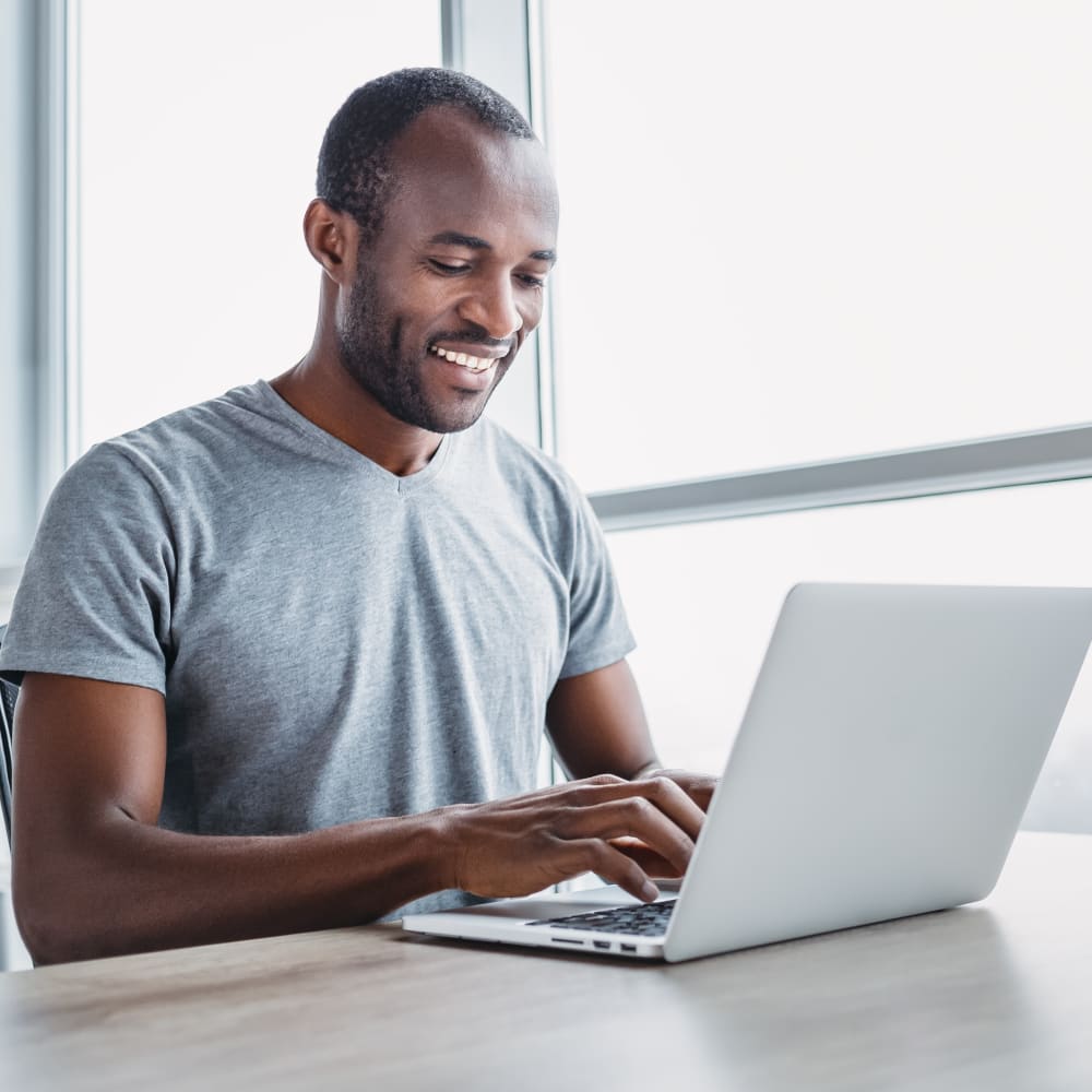 A man is smiling and working at a laptop.