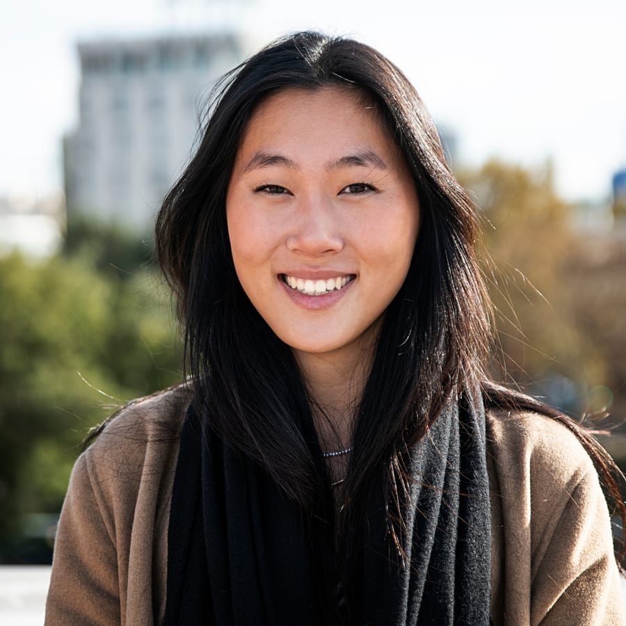 A woman wearing a brown sweater and a black scarf is smiling.
