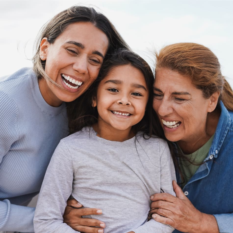 Two women are smiling at a young girl who is standing between them.