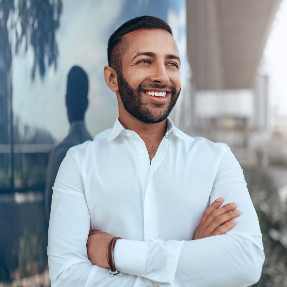 A man in a blue shirt is smiling with his arms crossed.