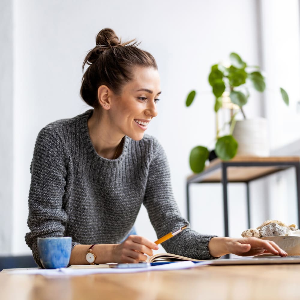 A woman in a grey sweater is working at a laptop.