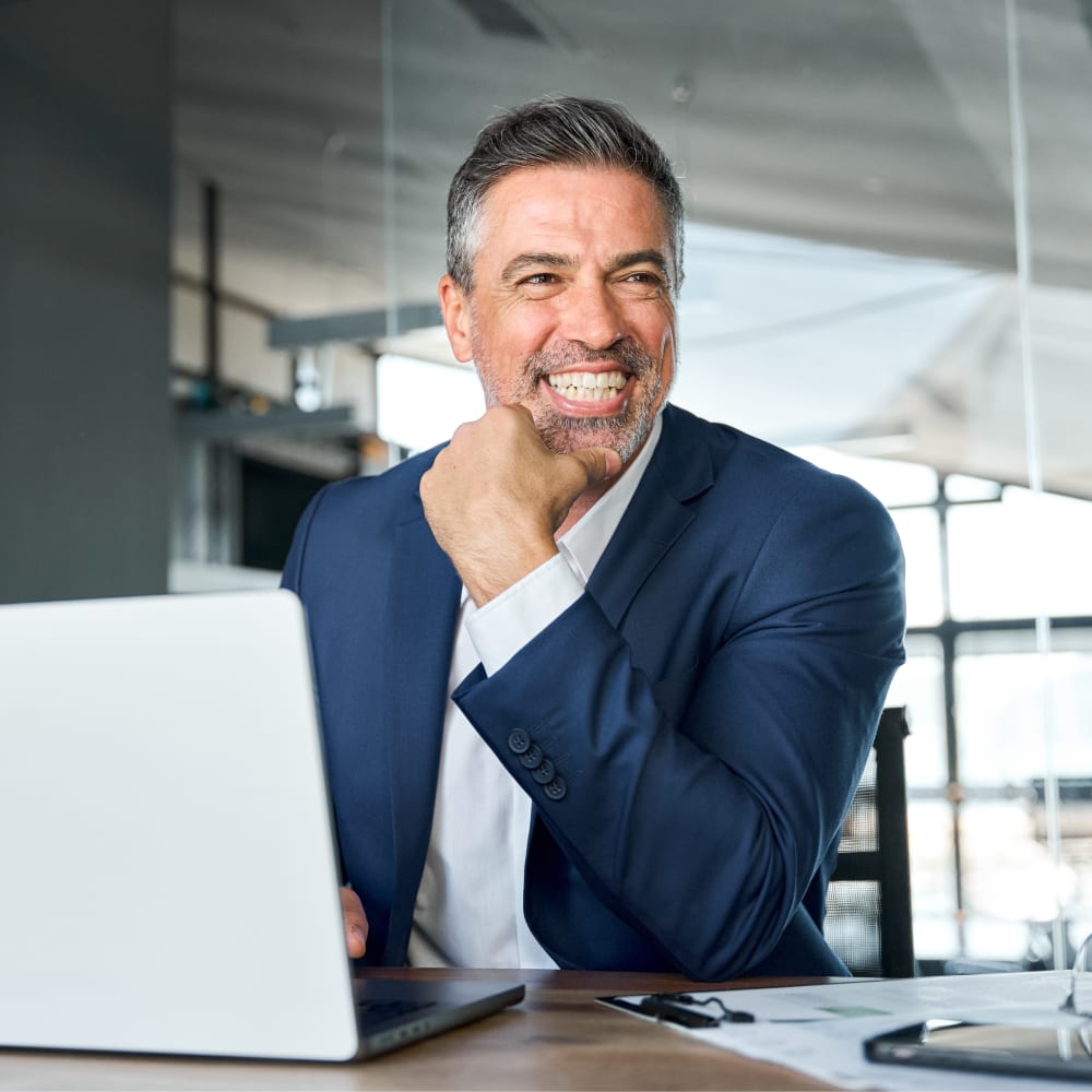 A man is smiling. In front of him is a laptop.