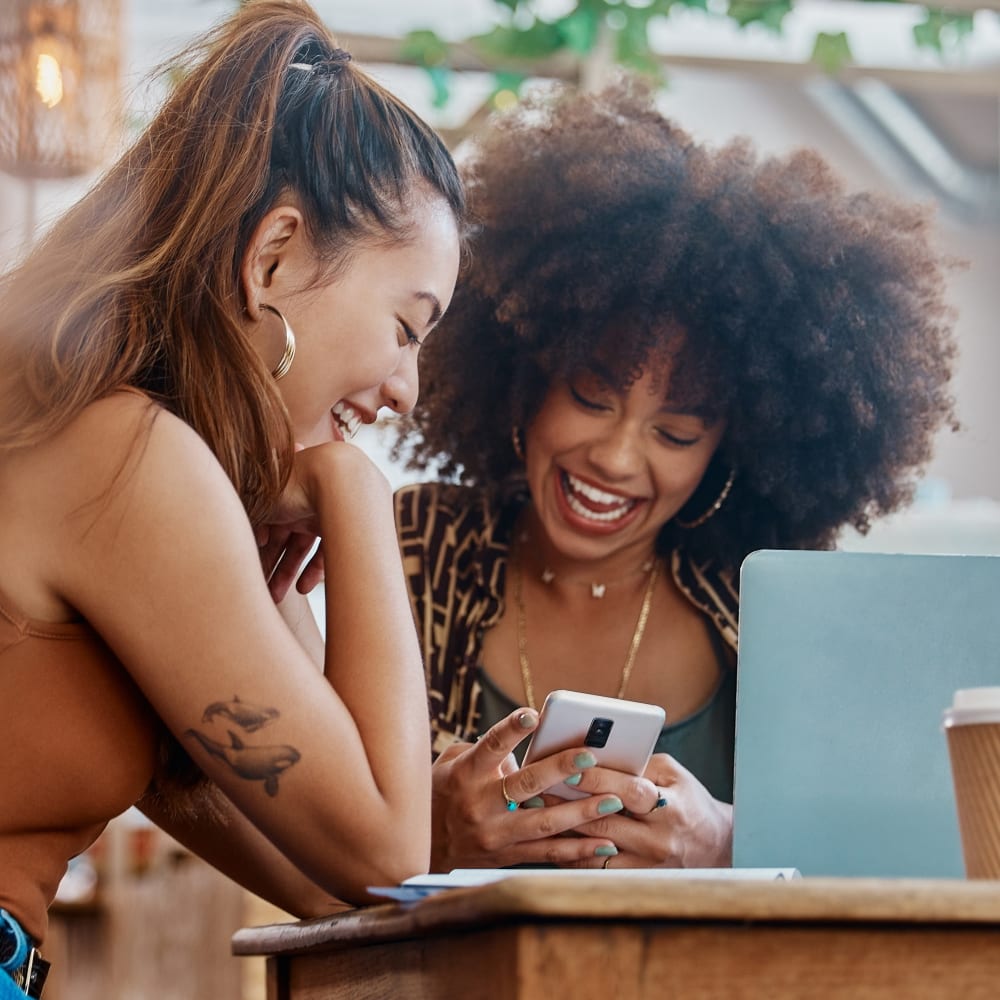 Two woman are looking at a smart phone together and laughing.