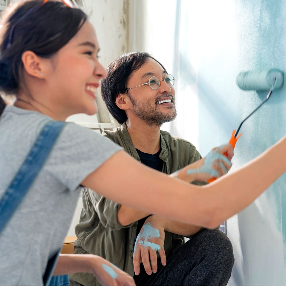 A man and a woman are crouched down together painting a wall.