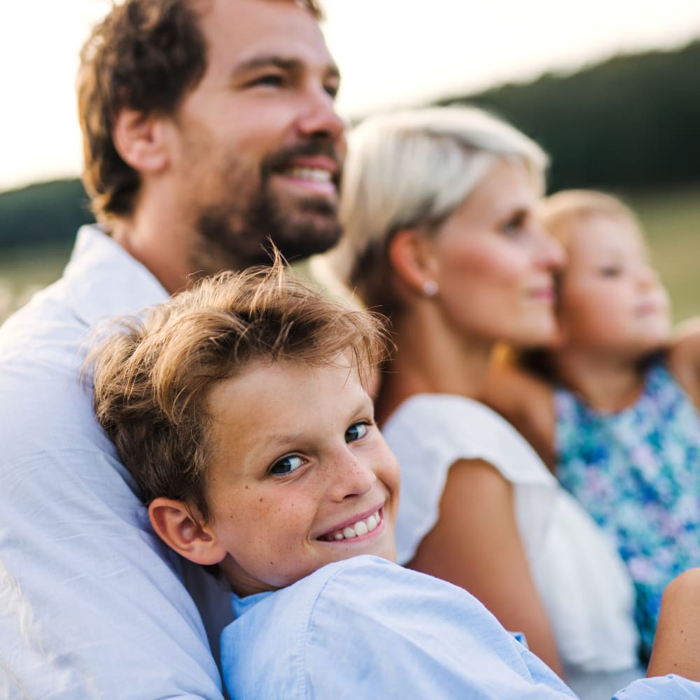 A family of four sits together outdoors, looking ahead while a young boy in the foreground looks directly toward the camera.