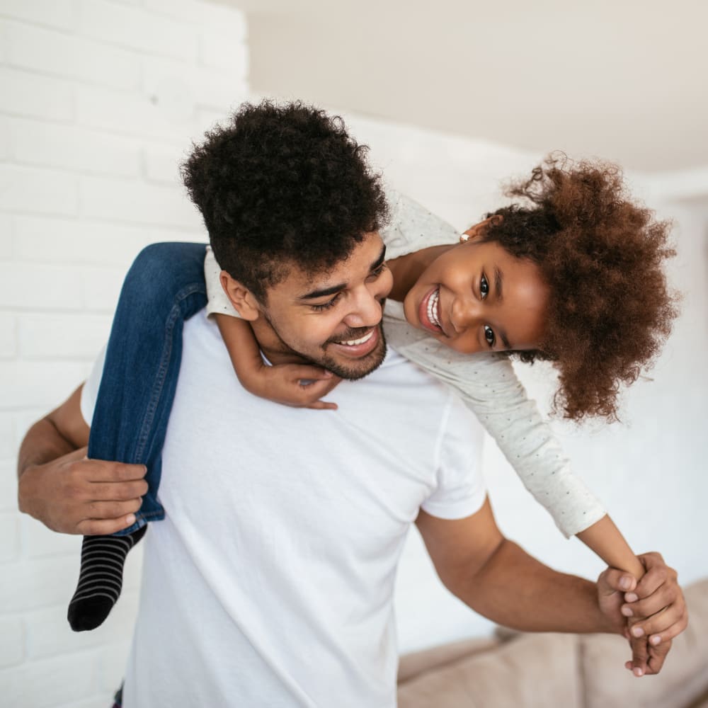 A man and young girl having fun, smiling as she climbs on his back.
