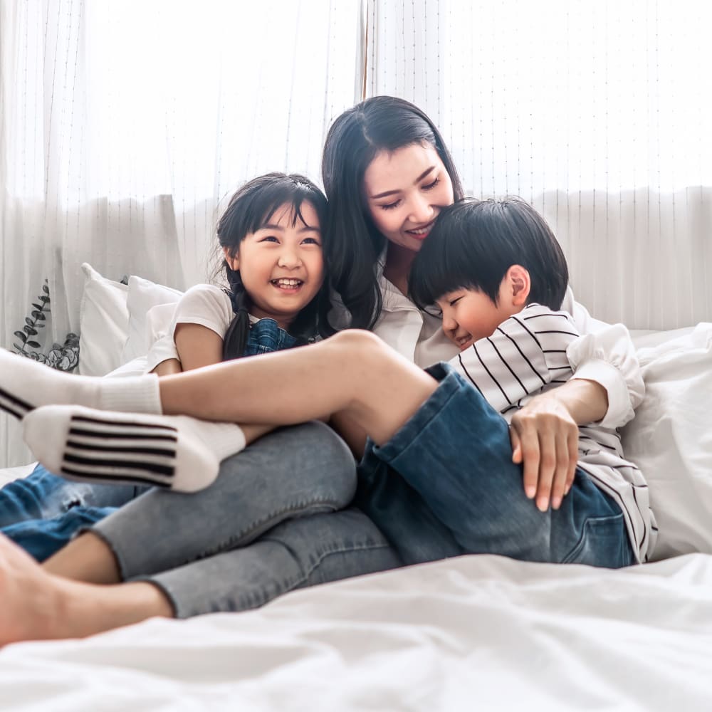 A woman is sitting on a bed hugging two kids.