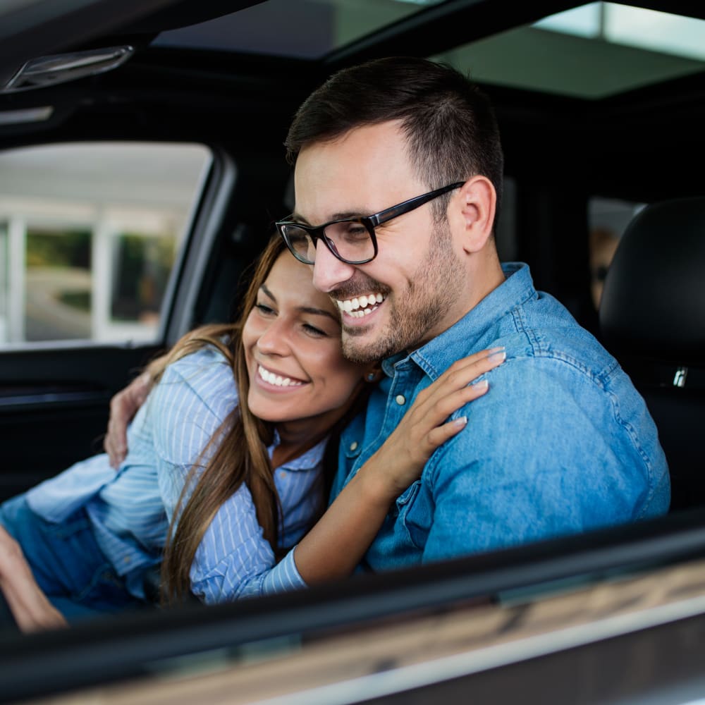 A couple are sitting in a car and smiling with their arms around each other.