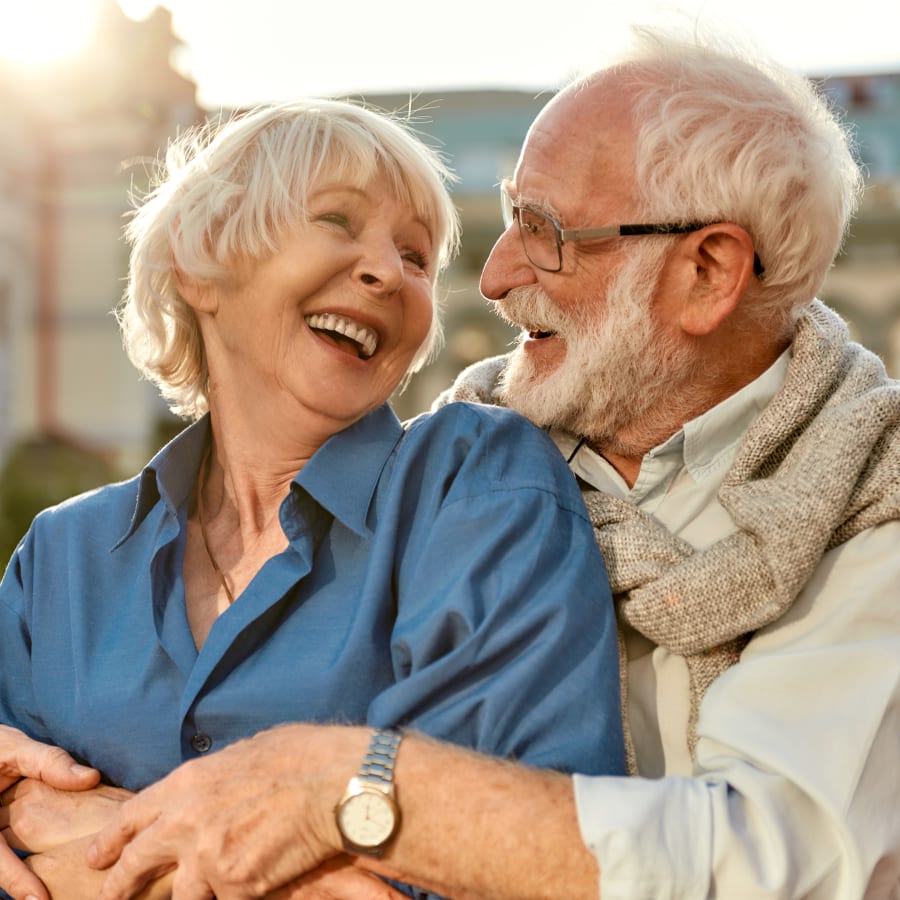 An older man and woman are laughing. His arms are around her.