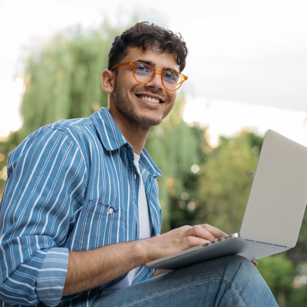 A man is sitting down with a laptop balanced on his legs.