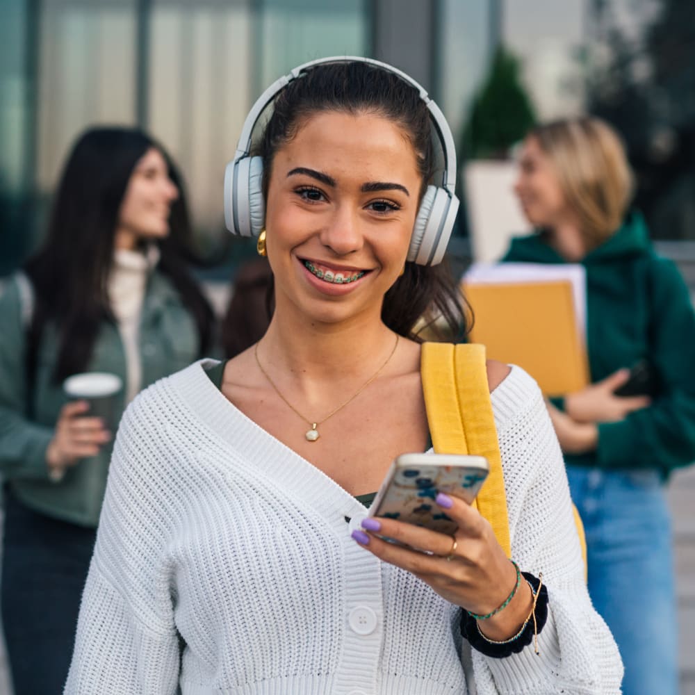 A girl is wearing headphones and using a smartphone. She is smiling and showing off her braces.