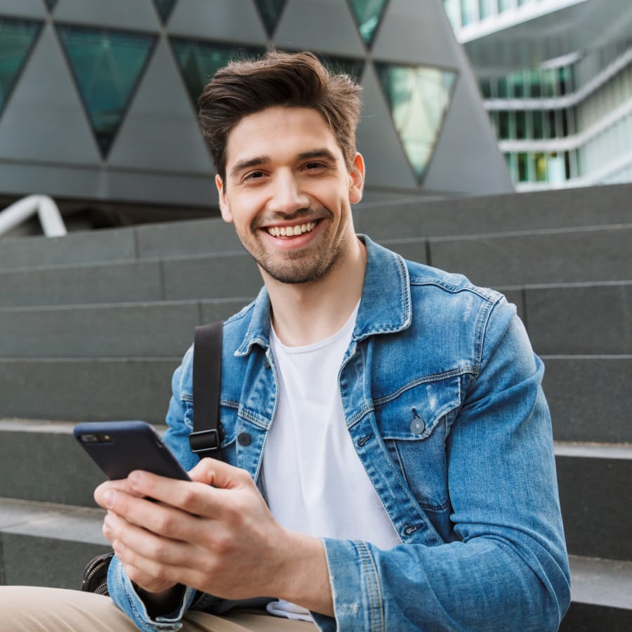 A young man is sitting on stairs outside and using a smartphone.