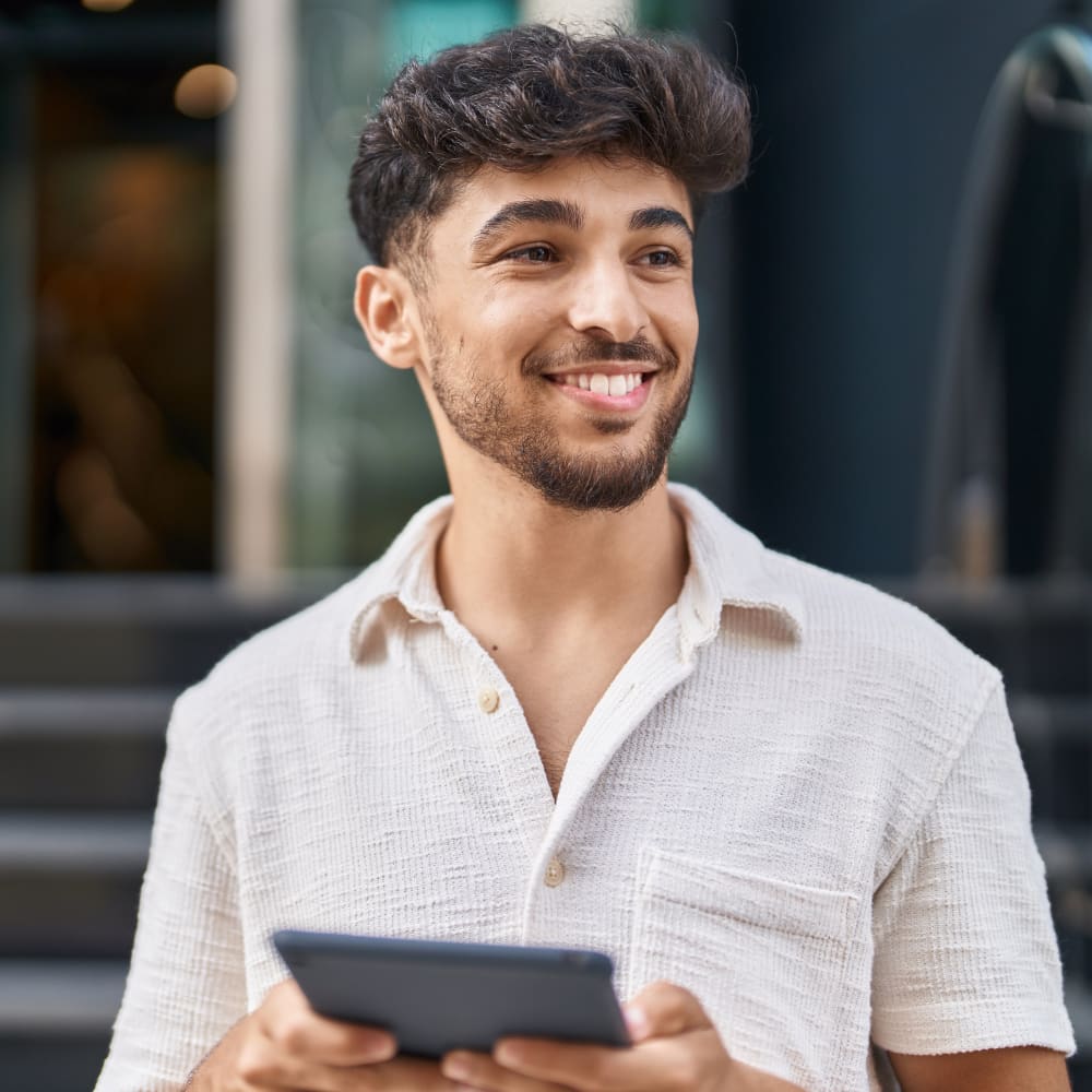 A young man is smiling and looking to the right. He has a tablet in his hands.