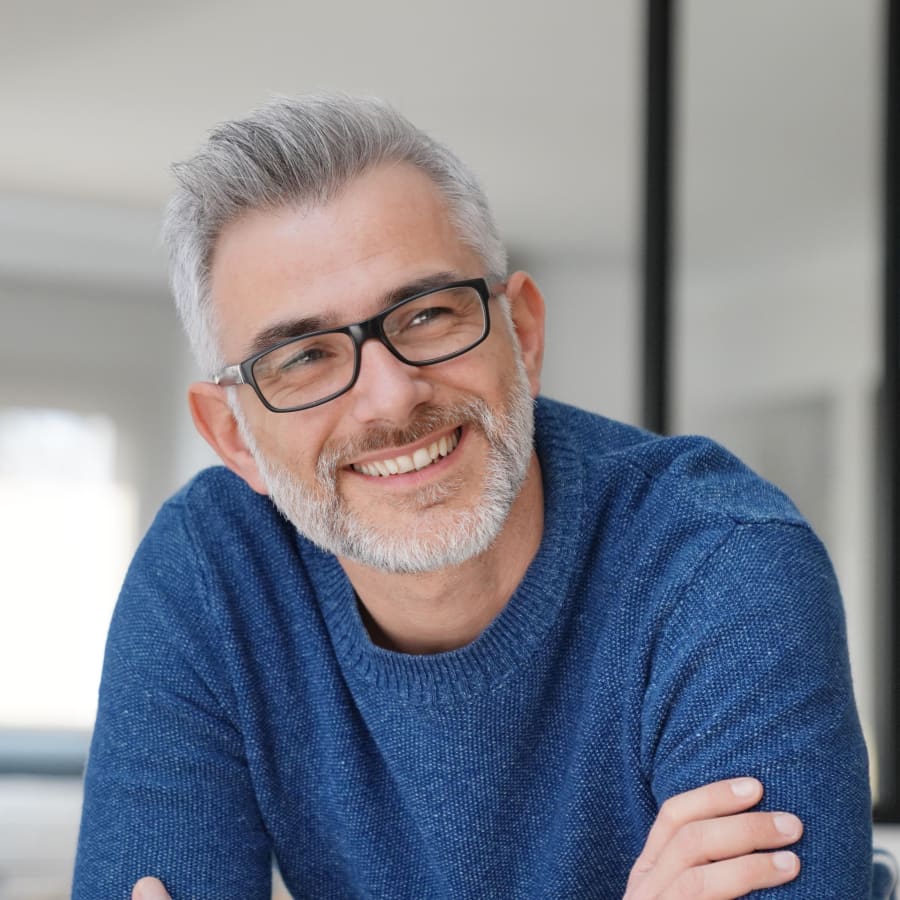 A man in a blue sweater and glasses is smiling.
