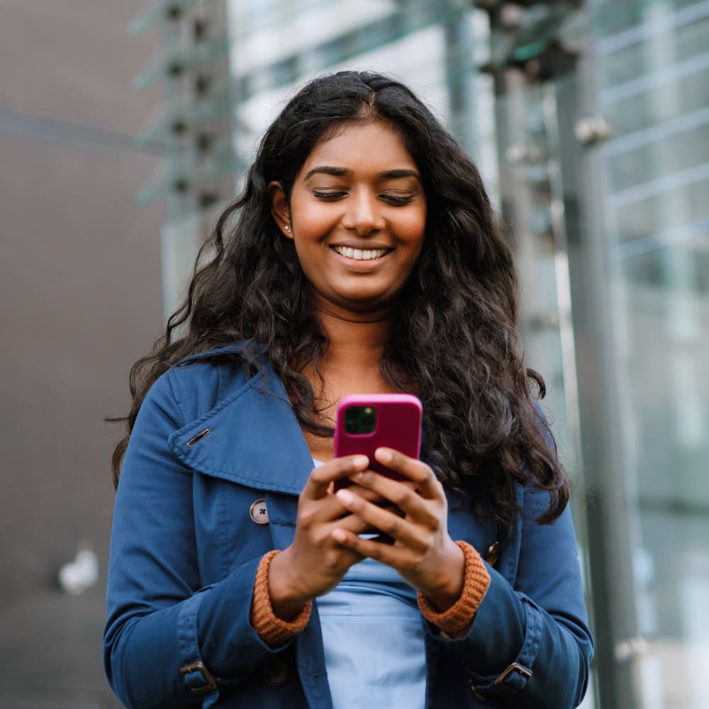 A woman wearing a blue jacket smiling while using her cellphone.